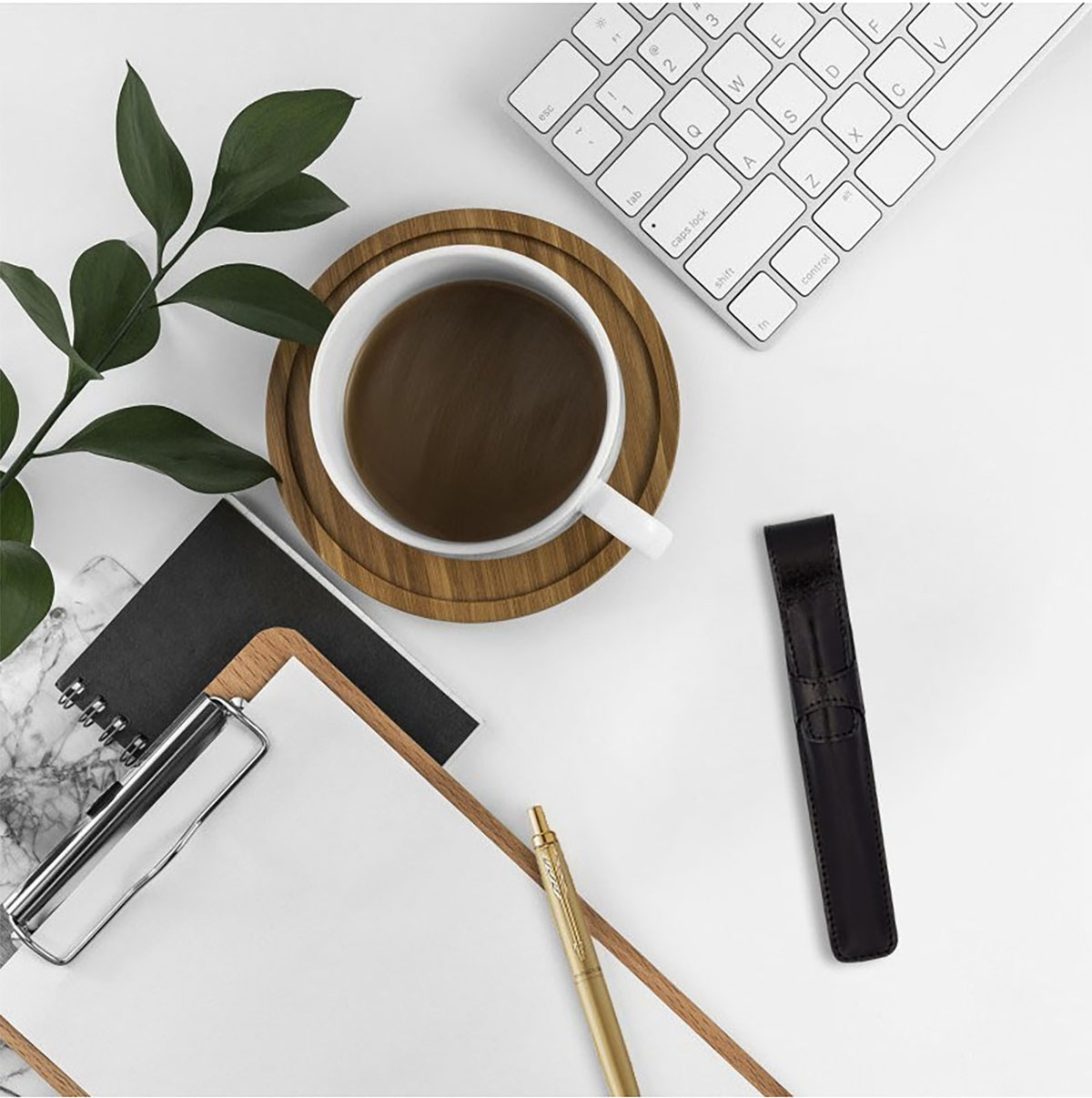 Biurko z filiżanką kawy, klawiaturą, notatnikiem i złotym długopisem obok czarnego etui na pióro.